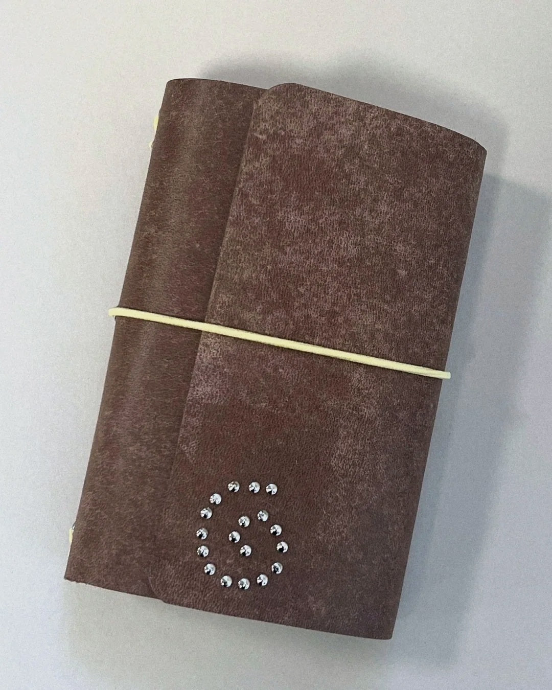 The Spiral Field Journal in brown patina leather with butter yellow elastic